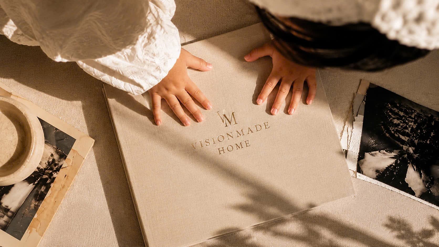 A child's hands resting on a linen VISIONMADE HOME memory album in warm morning light