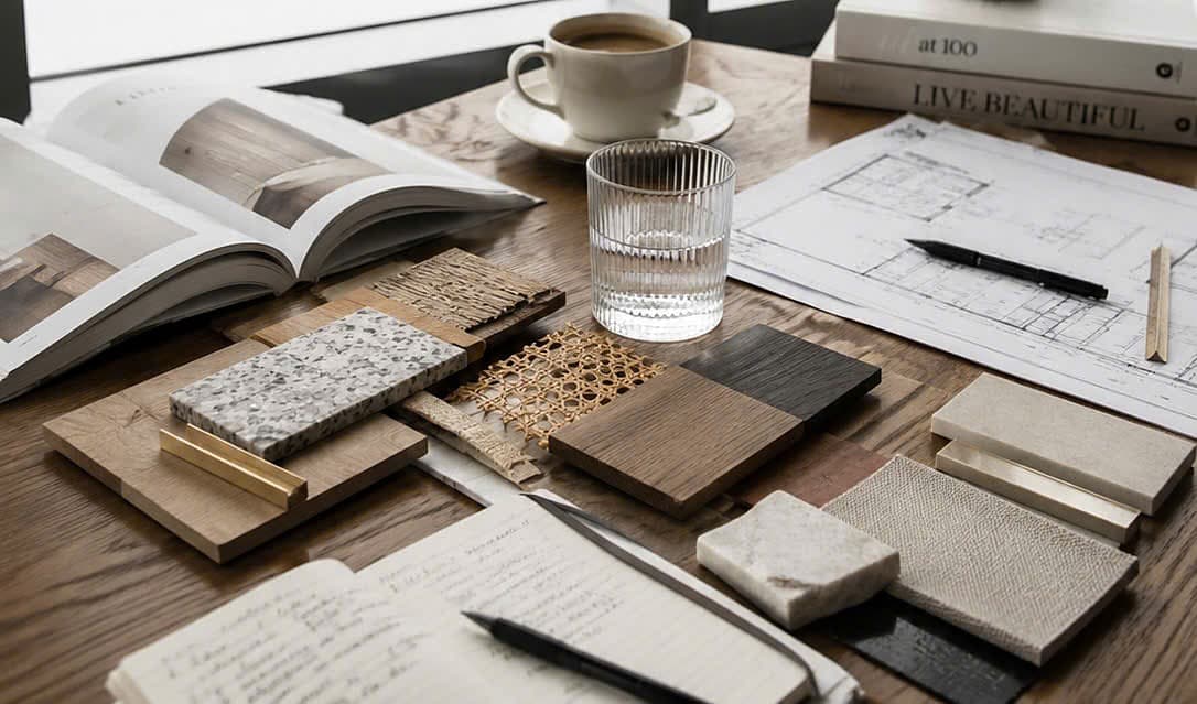 A flat-lay of stone, cane, oak and linen samples beside a coffee and floor plan